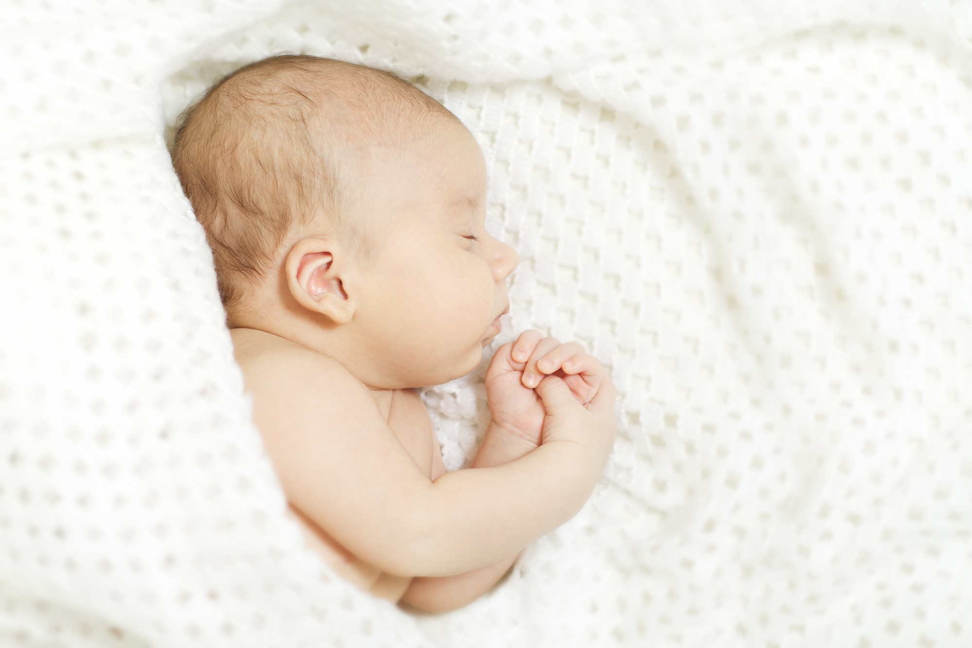 Newborn baby sleeping peacefully on a white knit blanket