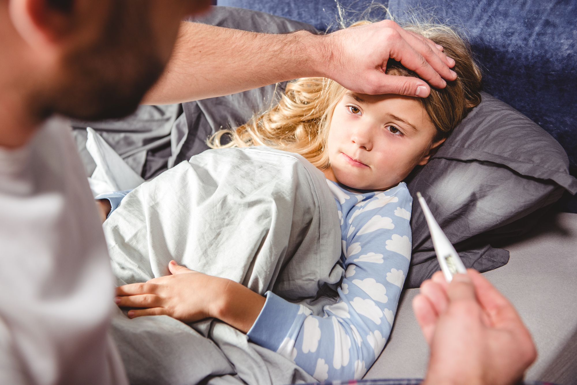 A concerned adult checking a sick child's forehead for fever while holding a digital thermometer