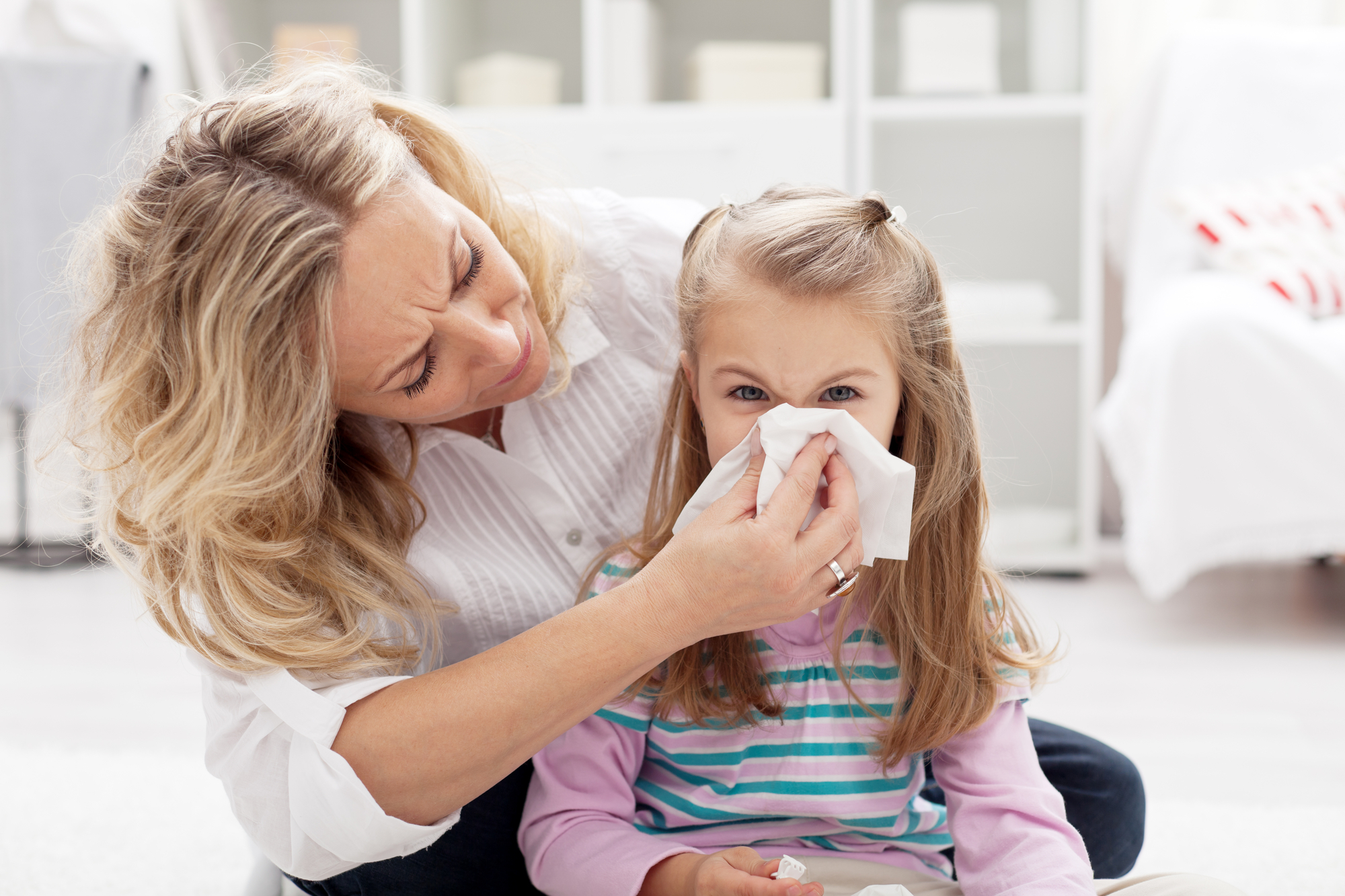 A woman helping a young girl blow her nose with a tissue
